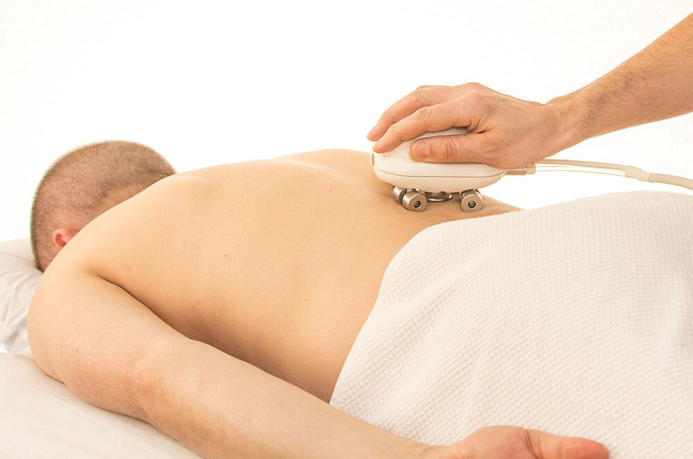 Man lying on massage table while a massage therapist rolls his back with a massager.