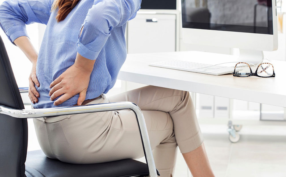 Woman sitting in office chair holding her lower back as if in pain
