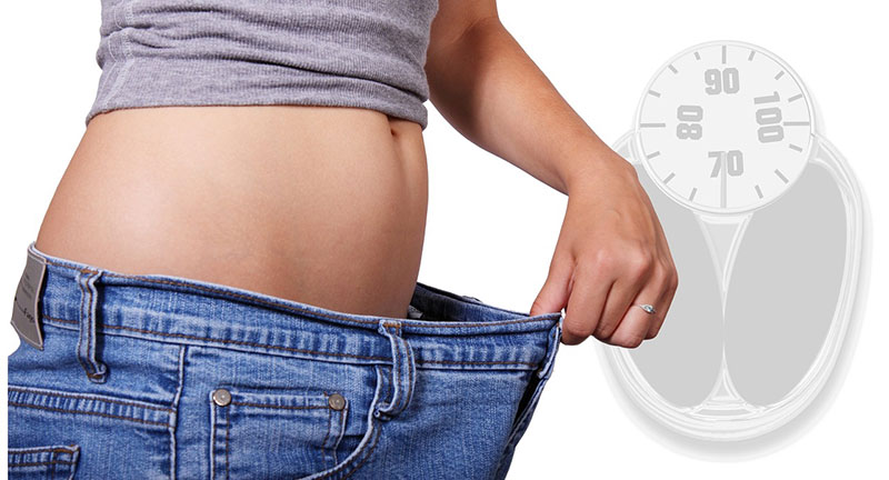 Woman pulling her pants out from her body to show weight loss with a graphic next to it showing a weight scale.