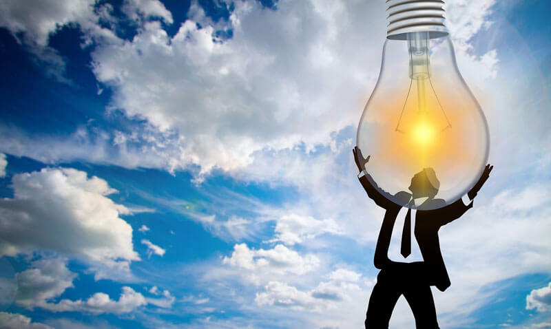 Man holding huge light bulb above his head and the light bulb is shining as if its getting energy from the sky