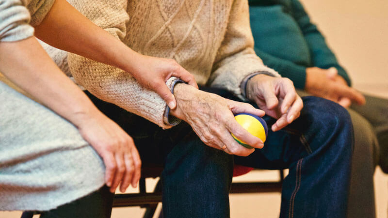 Elderly couple sitting on park bench holding hands. The focus is on the hands.