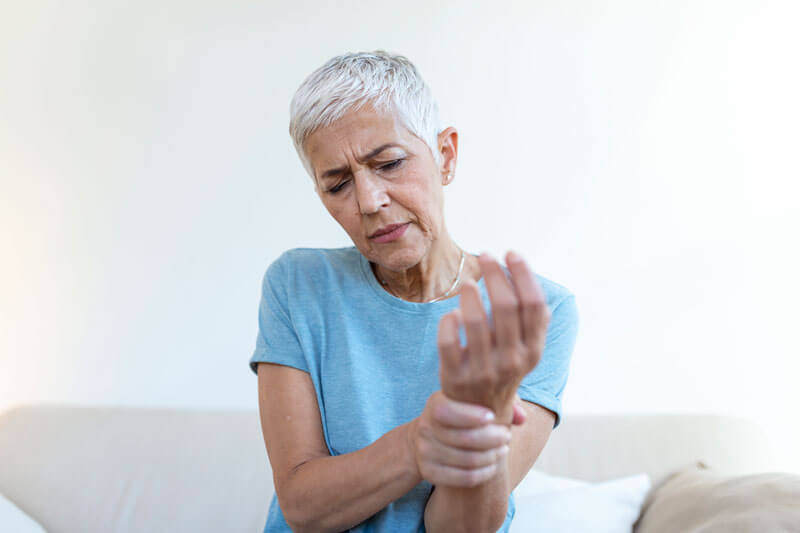 Elderly woman holding our her arm in pain, holding it with the other hand.