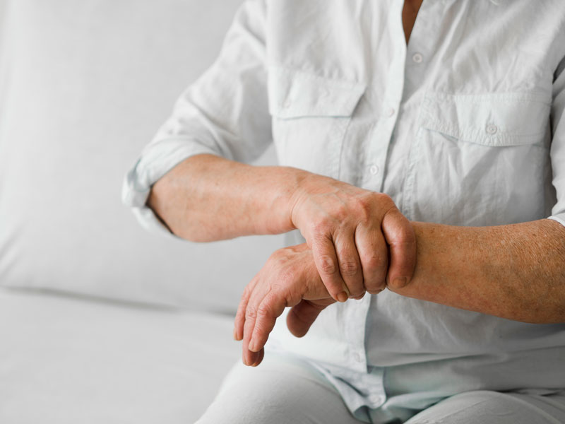 Older man sitting on couch with one hand on the other wrist as if in pain from arthritis.