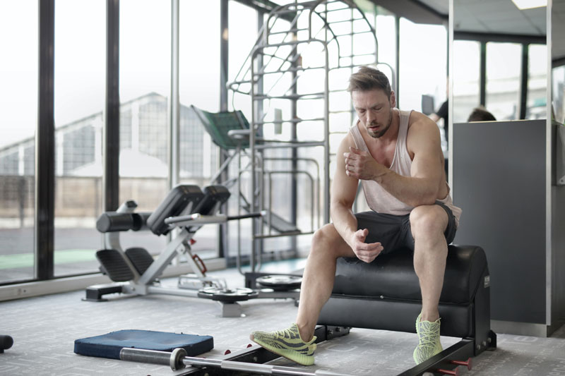 Man sitting in front of barbell in gym looking tired