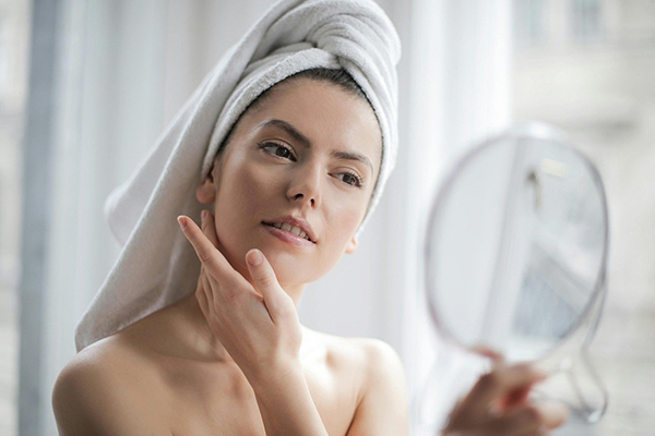 Woman with towel on head indicating she has just showered looking at herself in the mirror