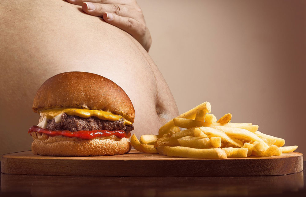 Man's stomach with a hamburger and french fries in the foreground