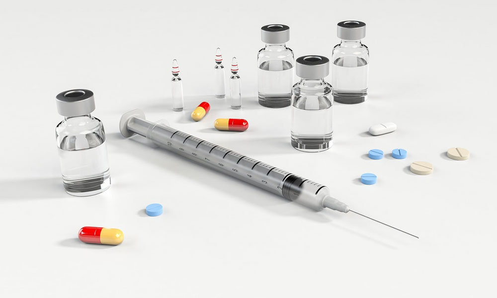 Medical syringe with needle on table with bottles of medicine surrounding it