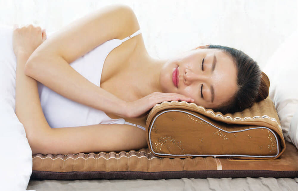 Woman from the neck up facing the camera with her eyes closed and a content look on her face with her head on an Amethyst Pillow and lying on a Biomat.