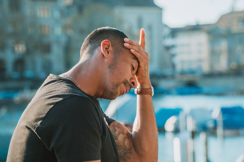 Man sitting outside with his head in his hand looking stressed.