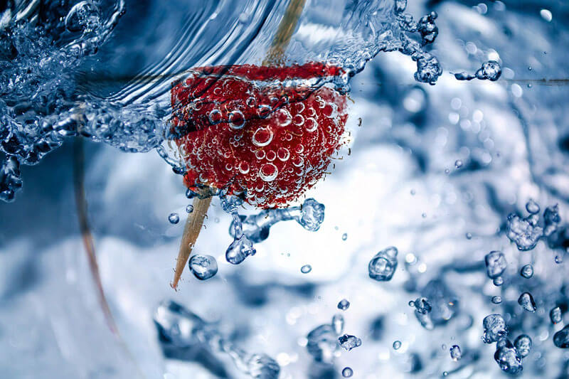 Water splashing out of a glass with a cranberry in it