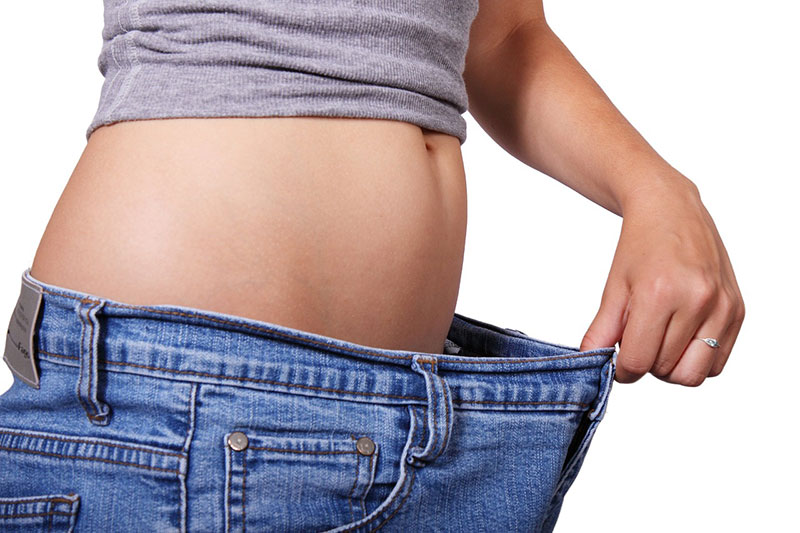 Woman's torso with hand pulling jeans away from stomach to show weight loss.